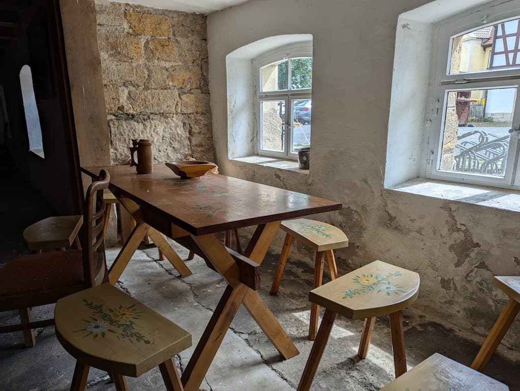 Das Bild zeigt einen alten Tisch und dazugehörige Hocker mit einem Blumendesign.